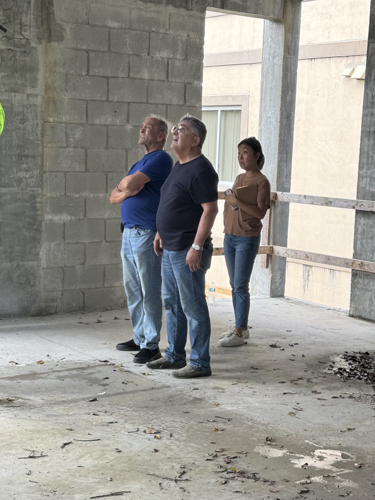La arquitecta en obra con los dueños-constructores, los tres mirando hacia arriba la estructura dentro de la cáscara de concreto sin terminar.
