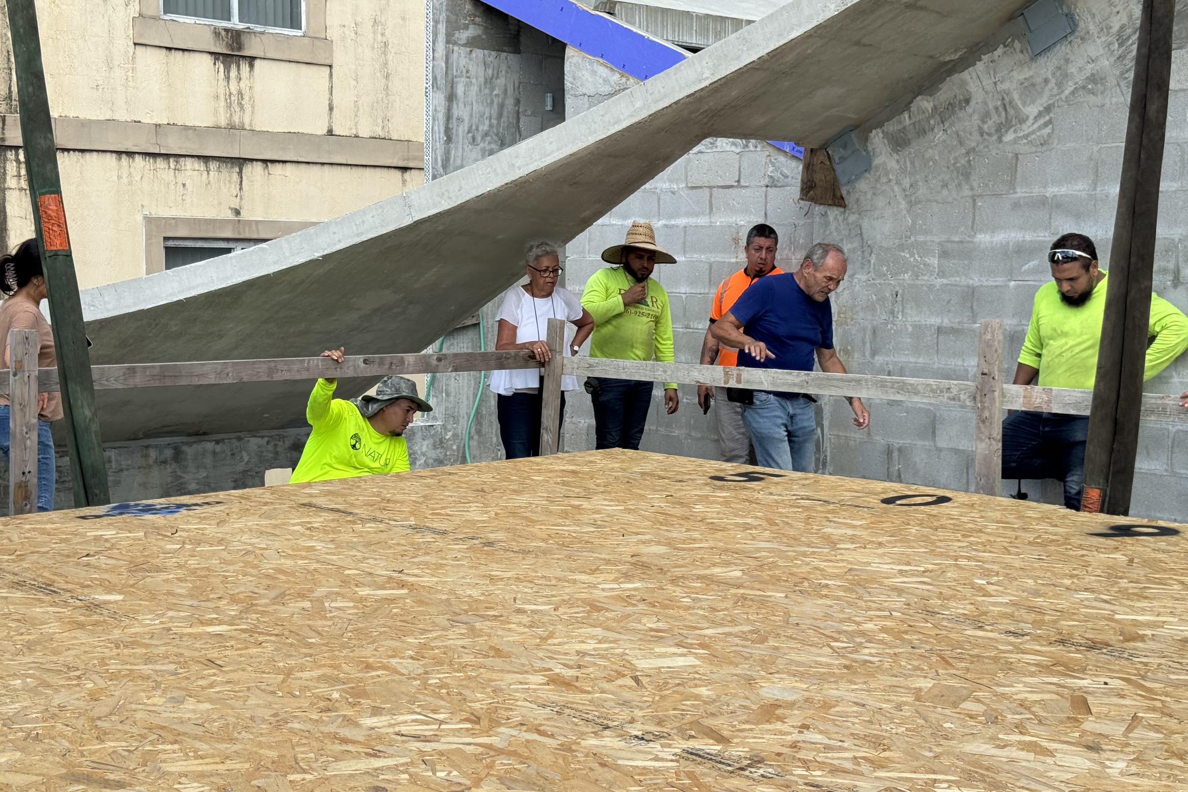 The crew working the deck as the precast panel is guided in. Leslie among them, blue polo, at the CMU wall. October…