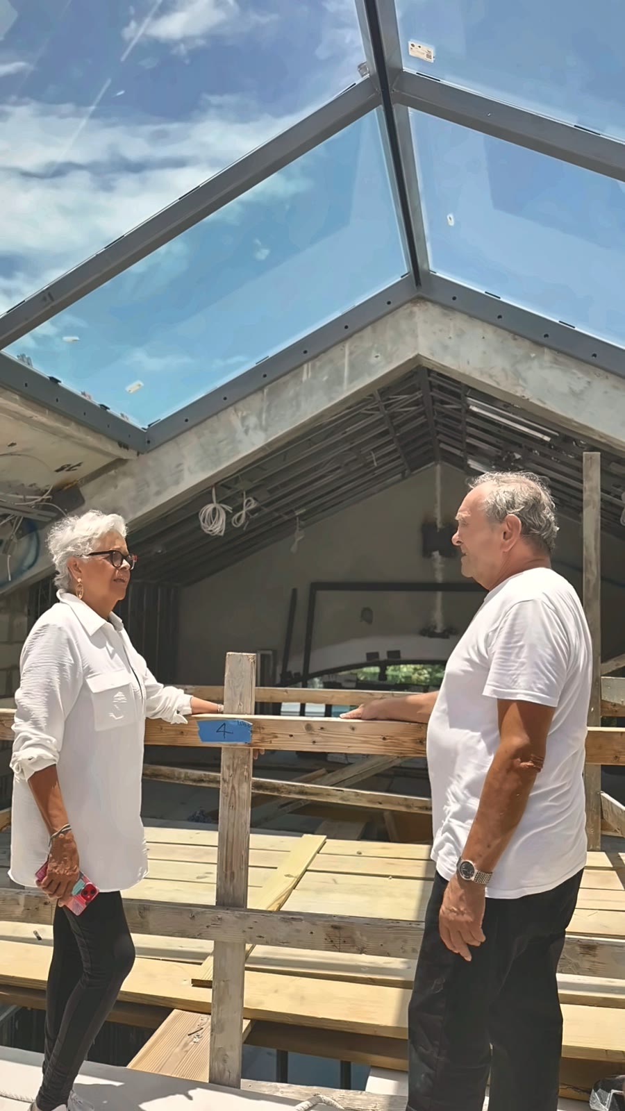 Leslie Gratz y Terry Matias en la losa bajo el tragaluz de vidrio, en conversación sobre una baranda de madera.
