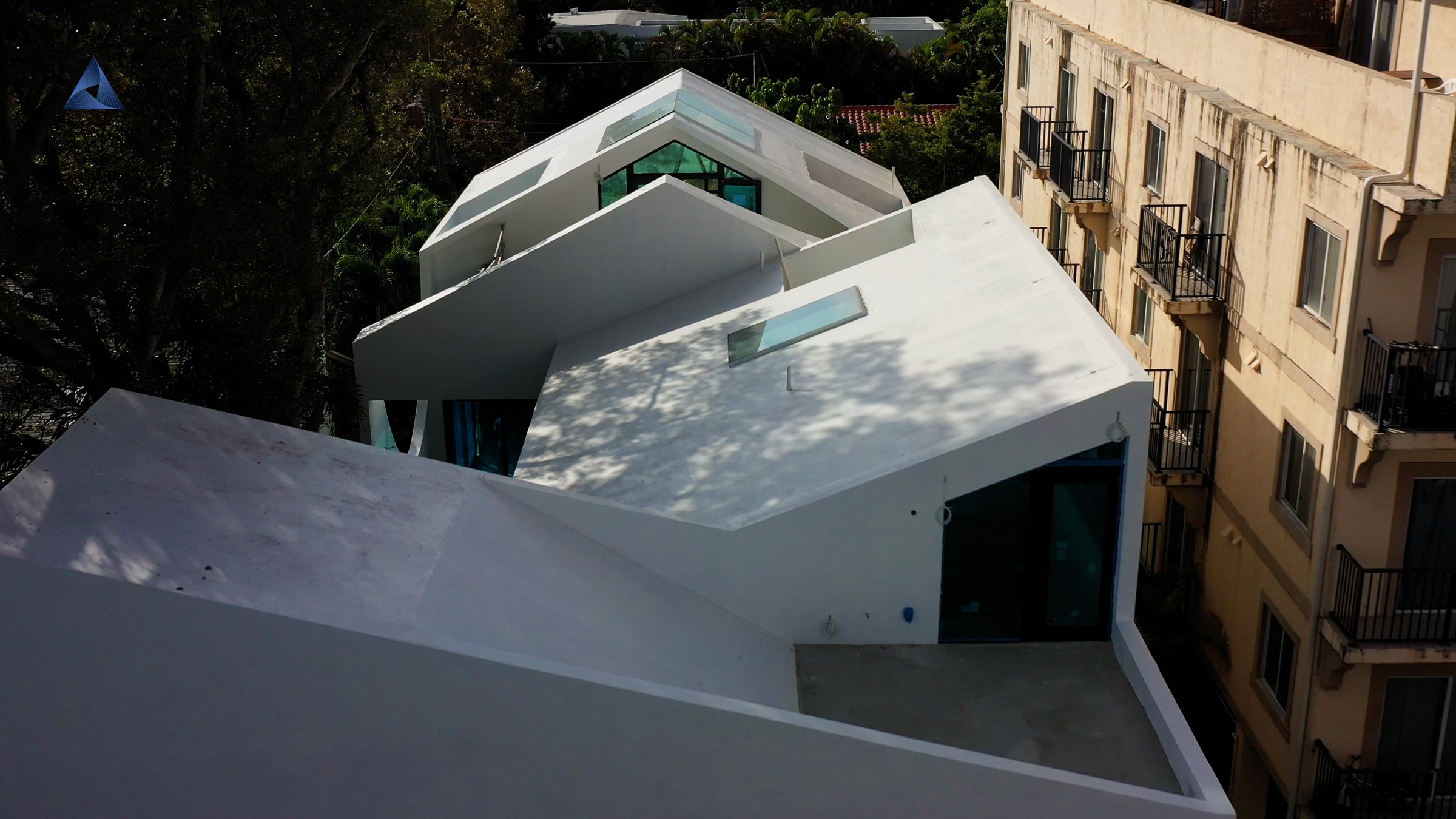 La casa en su manzana. Techos bajos y copa densa a ambos lados, y un volumen blanco escalonado en un solar intersticial…