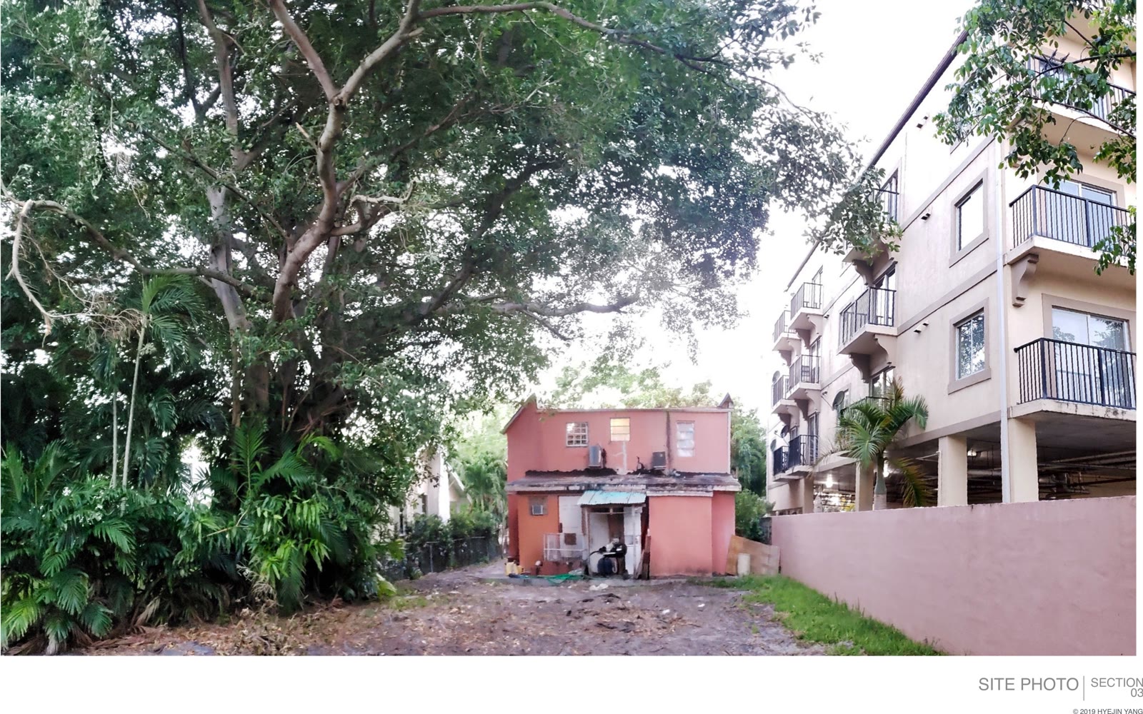 El solar antes de la casa: la construcción antigua tras su muro, un edificio de apartamentos pegado a un costado, y la…