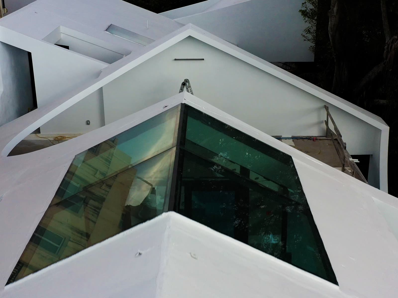 The lantern. A faceted glass volume set into the white roof plane — every facet is a penetration through a waterproofed…
