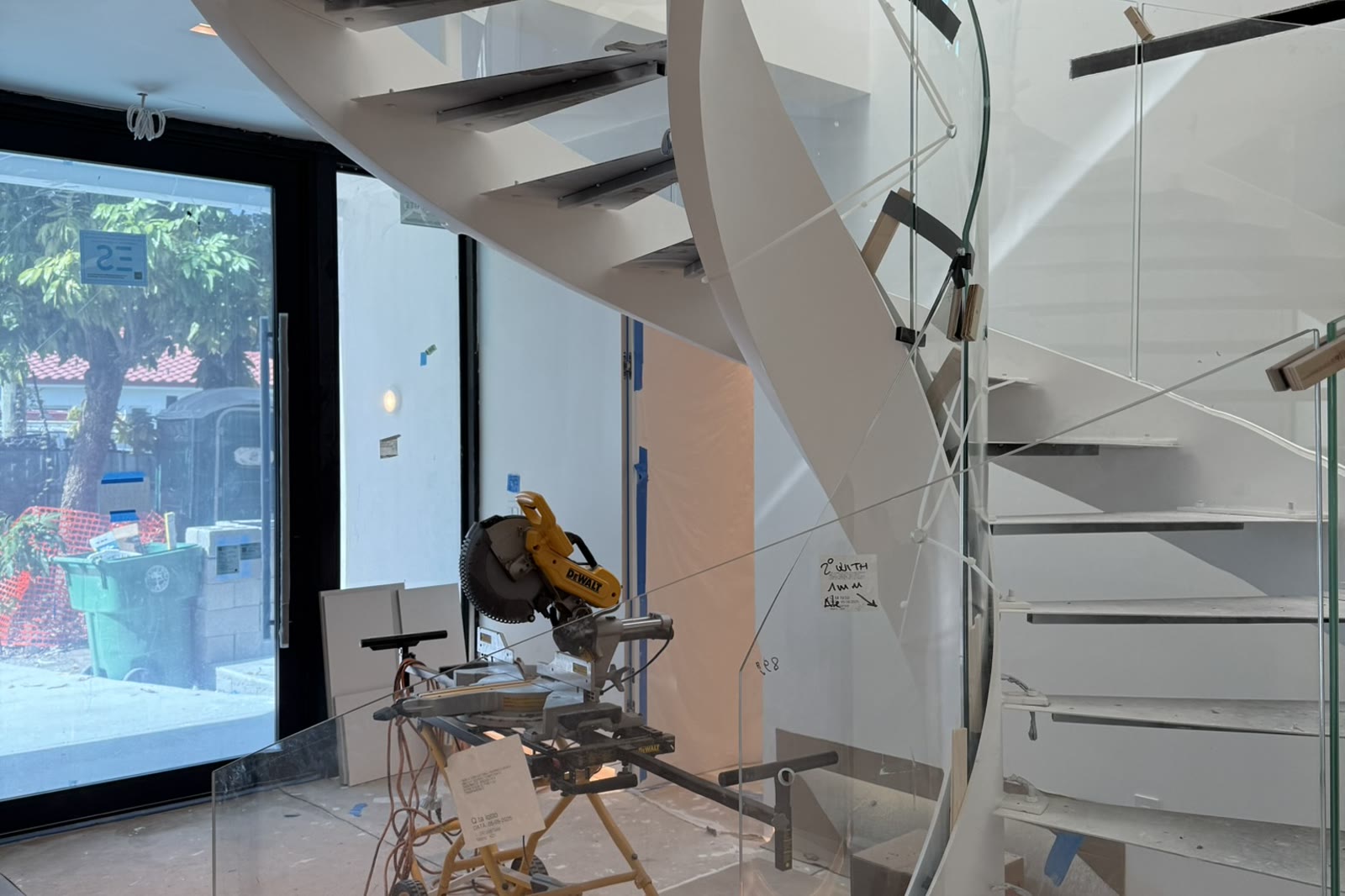 The finished stair: white spiral, glass balustrade, glazed wall behind. The result that the drawings had to earn.