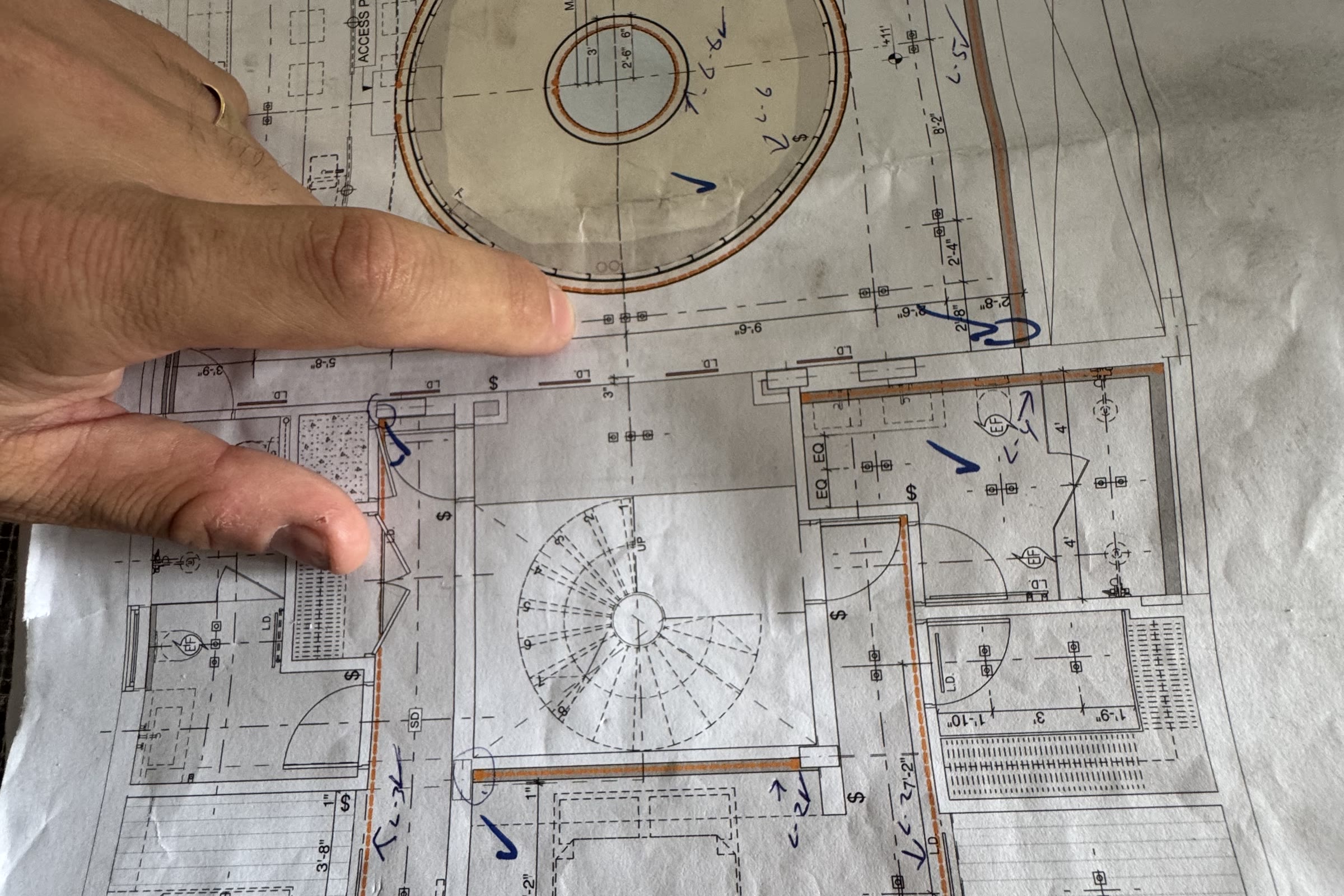 A plan sheet on a table, a hand resting on it. The circular stair is drawn in plan — the geometry that had to be right…